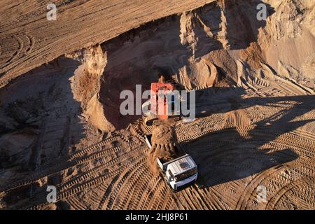 Der Bagger lädt den Sand in einen Muldenkipper im Tagebau. Entwicklung des Sandes im Tagebaus. Schwere Maschinen auf Erdarbeiten im Steinbruch. Miningtruck Stockfoto