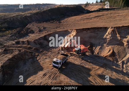 Der Bagger lädt den Sand in einen Muldenkipper im Tagebau. Entwicklung des Sandes im Tagebaus. Schwere Maschinen auf Erdarbeiten im Steinbruch. Miningtruck Stockfoto