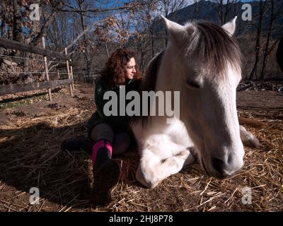 Seitenansicht des Weibchens in grüner Polar Fleece-Jacke, die an der Seite eines weißen Ponys sitzt. Stockfoto