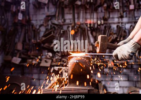 Authentischer Schmied schmiedet ein Metallprodukt in dunklen Innenräumen Studio Stockfoto