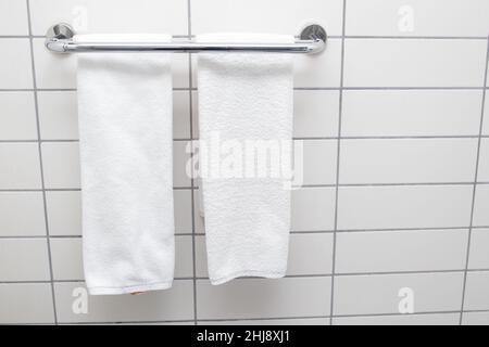 Beheizter Handtuchhalter an der Badezimmerwand. Weiße Handtücher trocknen auf einem beheizten Handtuchhalter Stockfoto