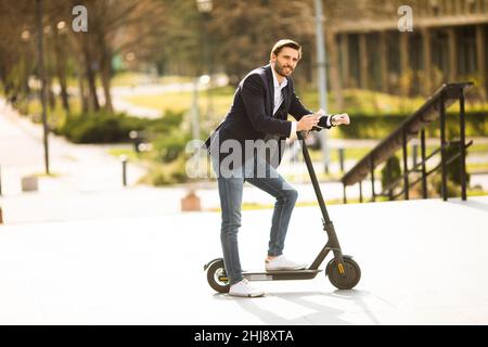 Schöner junger Geschäftsmann mit Handy auf Elektroroller Stockfoto