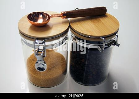 Nahaufnahme von zwei isolierten Glas- und Holzgläsern mit Kaffee und Rohrzucker mit einem Tischlöffel aus Kupfer und Holz Stockfoto