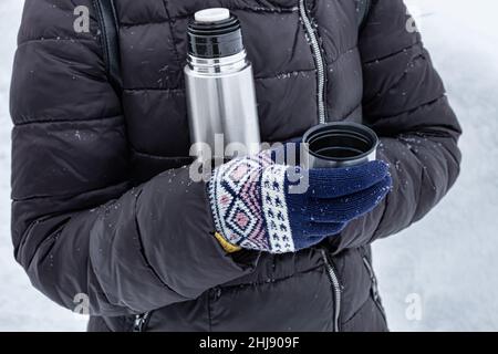 Frau, die im Winter ein Glas Tee aus einer Thermoskanne auf der Straße hält. Hochwertige Fotos Stockfoto