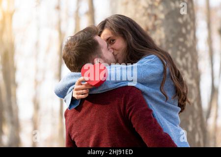 Der Mann überrascht seine Freundin mit einem herzförmigen Geschenk und sie küsst ihn Stockfoto