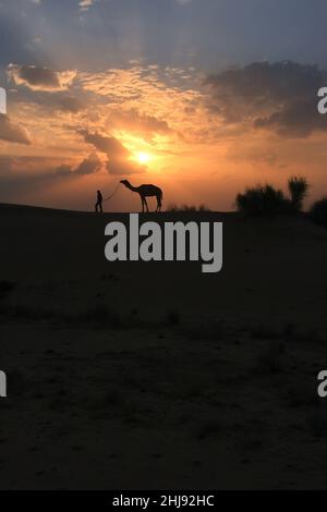 Silhouette Person mit einem Kamel bei Sonnenuntergang, Thar-Wüste in der Nähe von Jaisalmer, Rajasthan, Indien Stockfoto