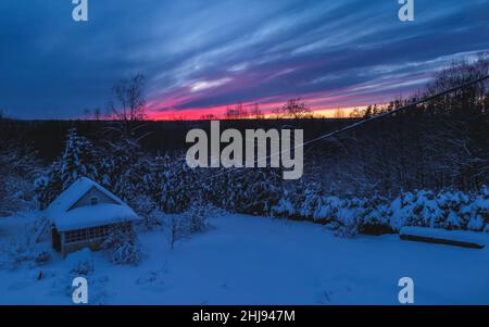 Waldhütte und Bäume im Winter Sonnenuntergang. Holzhütte im Schnee. Wald am Abendhimmel im Hintergrund. Stockfoto