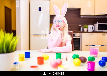 Nettes kleines Mädchen Malerei ostereier tragen Hasenohren in der Küche Stockfoto