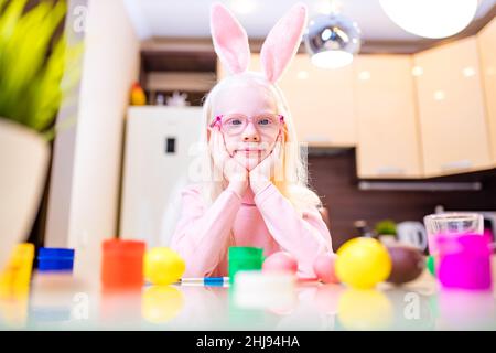 Nettes kleines Mädchen Malerei ostereier tragen Hasenohren in der Küche Stockfoto