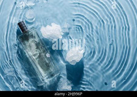 Parfüm-Flasche auf blauem Wasser gewellter Hintergrund mit Eisstücken. Frisches kühles Wasserduft-Konzept Stockfoto