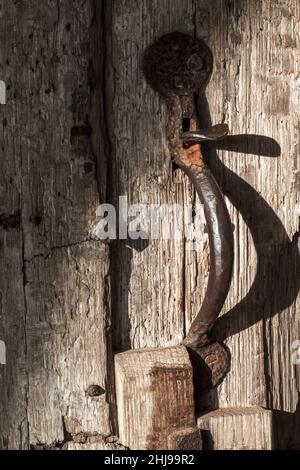 Robuster, vertikaler Türgriff aus Metall mit Daumenverriegelung an der alten Holztür Stockfoto