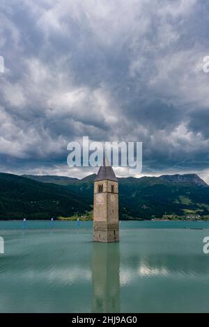 Der Glockenturm der Kirche St. Katharina ragt aus dem Wasser des Reservoirs Reschensee, bedeckt von dunklen Gewitterwolken. Stockfoto