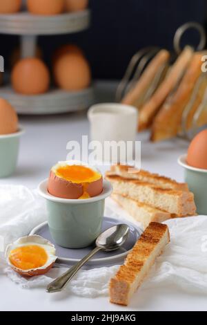 Ein Frühstückstisch mit frischen, weich gekochten Eiern mit runndem Eigelb in einer Eierschale mit Toastsoldaten Stockfoto