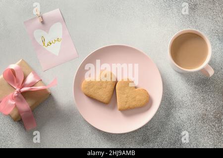 Herzförmige Kekse auf rosa Teller mit Kaffee und Geschenk zum Valentinstag. Draufsicht. Valentinstag Morgen mit Happy Love Frühstück. Stockfoto
