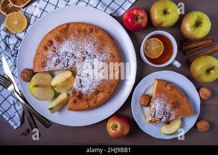 Draufsicht Nahaufnahme von Apfelkuchen in Scheiben mit Walnüssen und reifen Äpfeln. Stück Kuchen auf Teller und Tee mit Zitrone. Hausgemachte Kuchen mit Früchten der Saison. Se Stockfoto
