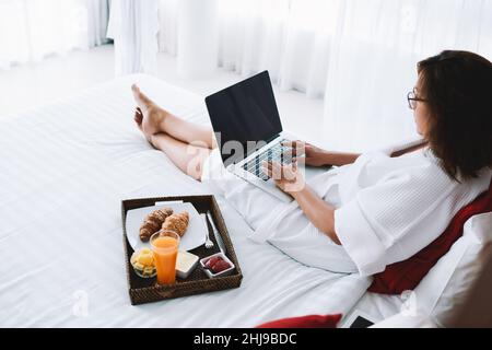 Junge Frau sitzt auf dem Bett mit laptop Stockfoto