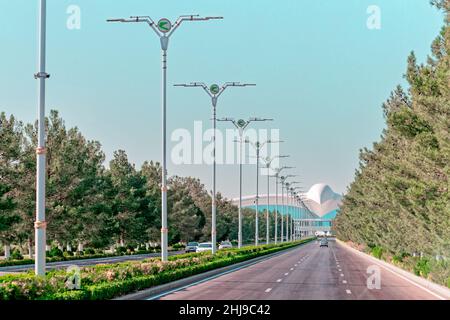 Stadtbild des Stadtzentrums von Ashgabat mit breiter Autobahn und leichtem Verkehr. Internationaler Flughafen Ashgabat im Hintergrund. Turkmenistan Stockfoto