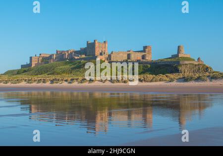 Die atemberaubende Burg von Bamburgh, Northumberland, aus dem Nordosten, vom Strand an einem Summers-Tag. Es spiegelt sich im Wasser wider. VEREINIGTES KÖNIGREICH Stockfoto