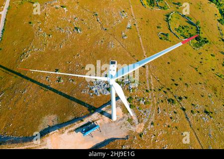 Die leistungsstarke Windenergieanlage mit großen Rotorblättern produziert an sonnigen Tagen auf der Bergspitze saubere erneuerbare Energie und schützt die Umwelt in der oberen Ansicht Stockfoto