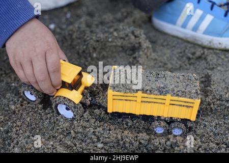 Die kleine Hand des Kindes spielt mit einem Traktor im Dreck Stockfoto