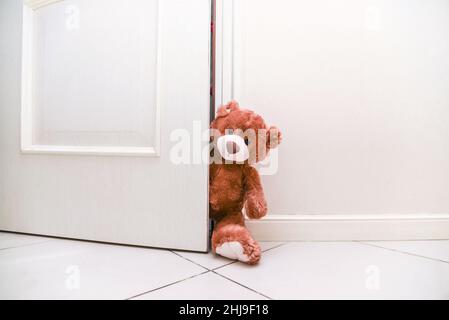 Stofftier Teddybär hinter offener Tür. Hintergrund für Kinder spielen. Platz auf weiße Tür und Wand kopieren. Stockfoto