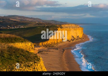 Burton Bradstock, Dorset, Großbritannien. 27th. Januar 2022. Wetter in Großbritannien. Am späten Nachmittag erhellt die Sonne die goldenen Sandsteinklippen und den Strand von Burton Bradstock an der Dorset Jurassic Coast, während die Wolken am Tag von überdurchschnittlichen Temperaturen kurz vor Sonnenuntergang klar werden. Bildnachweis: Graham Hunt/Alamy Live News Stockfoto