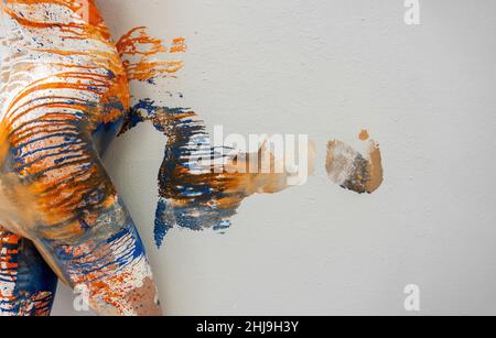 Junge künstlerisch abstrakt gemalte Schwangere mit orange, blau, weiß, Farbe, rollt ihren großen runden Bauch auf die Studiowand, so dass künstlerische Spalte Stockfoto
