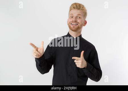 Happy junge Rotschopf Kerl mit roten stilvollen Bart isoliert. Mann, der auf den Kopierplatz für Werbung zeigt. Männlich in schwarzem Hemd, Trend-Haarschnitt. Erfolgreiche junge Menschen Stockfoto