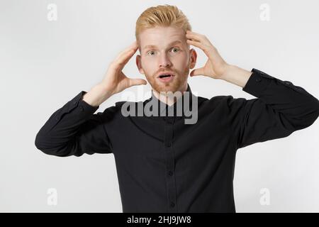 Schockerregt rothaarigen jungen Mann mit rotem Bart mit Wow Emotionen. Kerl in schwarzem Hemd isoliert. Emotionales männliches Gesicht aus nächster Nähe. Person Portrait Stockfoto