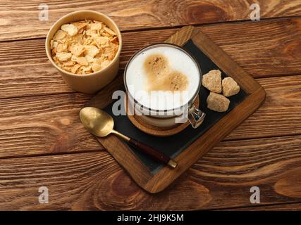 Nahaufnahme einer Tasse Cappuccino-Kaffee mit herzförmiger Latte-Kunst und Napoleon mille-feuille-Vanillepudding-Torte auf schwarzem Schiefer über Holz Stockfoto