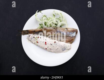 Close up Teil Salzwasser eingelegte Hering Fischfilets mit Zwiebeln und Soße auf weiße Platte über schwarzen Tisch, Erhöhte Ansicht von oben, direkt über Stockfoto