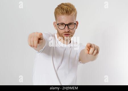 Kerl zeigt auf Sie durch Finger isoliert auf weißem Hintergrund. Junger stilvoller rothaariger Mann, roter Bart und Brille. Weißes T-Shirt zeigt sich auf dir. Erfolg A Stockfoto