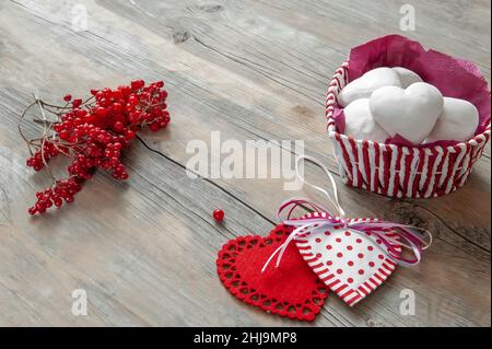 Herzen aus Stoff auf einem hölzernen Hintergrund mit weißem Lebkuchen in Form eines Herzens. Ein Herz aus verschiedenen Arten von handgefertigten Stoff gewebt ist Stockfoto