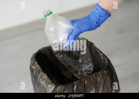 Frau trägt Gummihandschuhe werfen leere Plastikflasche auf den Papierkorb. Stockfoto