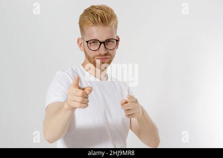 Kerl zeigt auf Sie durch Finger isoliert auf weißem Hintergrund. Junger stilvoller rothaariger Mann, roter Bart und Brille. Weißes T-Shirt zeigt sich auf dir. Erfolg A Stockfoto