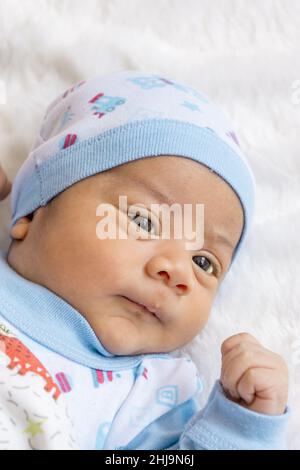 Entzückendes lateinisches Baby, das sich hinlegt, einen Hut und Bettwäsche trägt, neugeborener Lebensstil, neues Leben und die Pflege des Säuglings mit Liebe im Studio Stockfoto