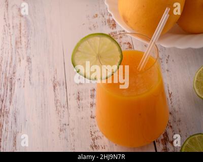 Foto zeigt Glas transparent mit natürlichem frischen Mango-Saft Nahaufnahme auf vintage strukturiert. Im Hintergrund sind exotische gelbe Mangofrüchte zu sehen. Stockfoto