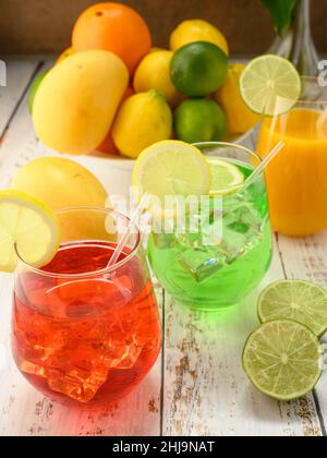 Foto zeigt verschiedene frische Früchte wie Mangos, Zitronen, Limetten und Orangen. In der Mitte des fotos befinden sich 3 Mocktails auf einem weiß getündelten Tisch in einem Glas mit einem W Stockfoto