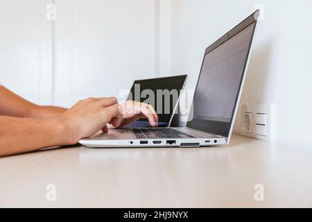 Seitenansicht eines Arbeitsbereichs zu Hause mit zwei Computern, einem an- und einem aus und die Hände eines Mannes, der tippt. Menschen nicht erkennbar. Speicherplatz kopieren Stockfoto