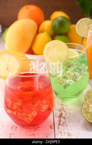 Foto zeigt verschiedene frische Früchte wie Mangos, Zitronen, Limetten und Orangen. In der Mitte des fotos befinden sich 3 Mocktails auf einem weiß getündelten Tisch in einem Glas mit einem W Stockfoto