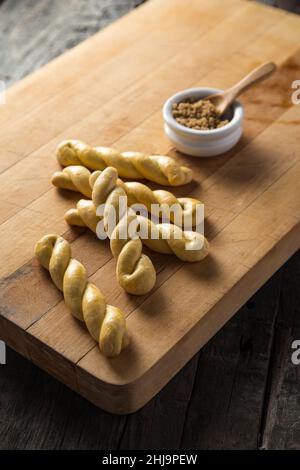 Eine Frühstücksplatte aus gebackenem Brotstock wird mit einer Schüssel braunem Zucker auf einer schwarzen Holzplatte verdreht. Stockfoto