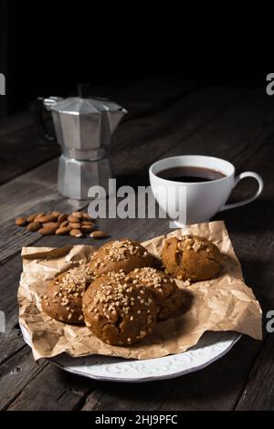 Ein Frühstücksteller aus gebackenen Walnussmuffins, dunklem Kaffee und Mandelnüssen, der auf einer schwarzen Holzplatte platziert ist. Stockfoto