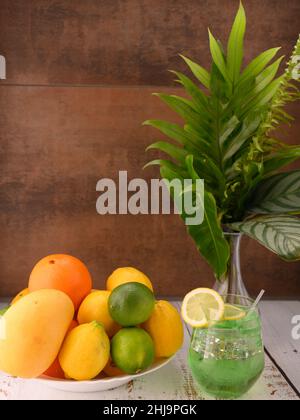 Das Foto zeigt eine Mischung aus Früchten wie Mangos, Zitronen, Limetten und Orangen. In der Mitte von foto ist 1 Kiwi Mocktails auf dem Tisch in einem Glas mit einem Keil von Stockfoto