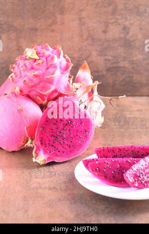 Foto zeigt vegane Ernährung wie Pitahaya Frucht des Kaktus. Rosafarbener Hintergrund. Bio-exotische Früchte auf braunem Muster. Stockfoto