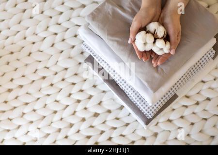 Gut gepflegte Frau Hände halten die Baumwollzweig mit Haufen Von gefalteten Bettlaken und Decken Stockfoto