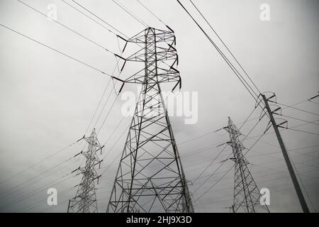 Hohe elektrische Hochspannungsleitungen aus Metall vor einem grauen Wolkenhintergrund. Stockfoto