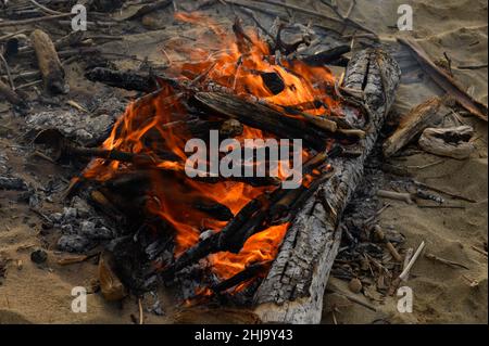 Das Foto zeigt, wie das Feuer brennt, Zungen aus orangefarbenem Faden platzen aus dem brennenden Holz. Kamin befindet sich in grüner Wiese. Abb. Stockfoto