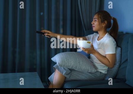 asiatische Frau Fernsehen Spannung Film oder Nachrichten schauen glücklich und lustig und essen Popcorn spät in der Nacht zu Hause Wohnzimmer Couch während der Zeit der Stockfoto
