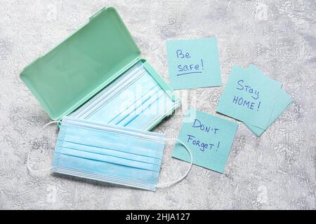 Medizinische Masken, Haftnotizen mit Text BLEIBEN ZU HAUSE, SEIEN SIE SICHER und VERGESSEN Sie NICHT auf grunge Hintergrund Stockfoto