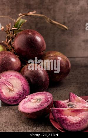 Foto zeigt mehrere lila tropische Früchte. Eine Frucht wird aufgeschnitten und das Innere ist sichtbar. Caimito Fruit stammt aus dem Dschungel der Dominikanischen Repu Stockfoto